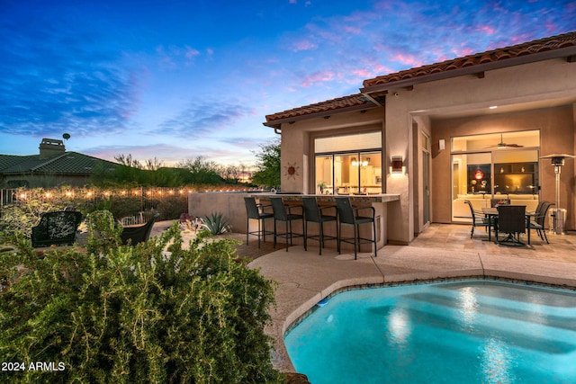 pool at dusk featuring an outdoor bar and a patio