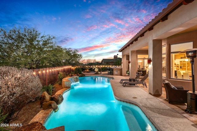 pool at dusk with pool water feature and a patio area