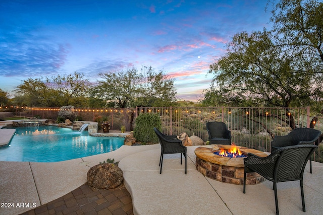 pool at dusk with an in ground hot tub, pool water feature, a patio, and an outdoor fire pit