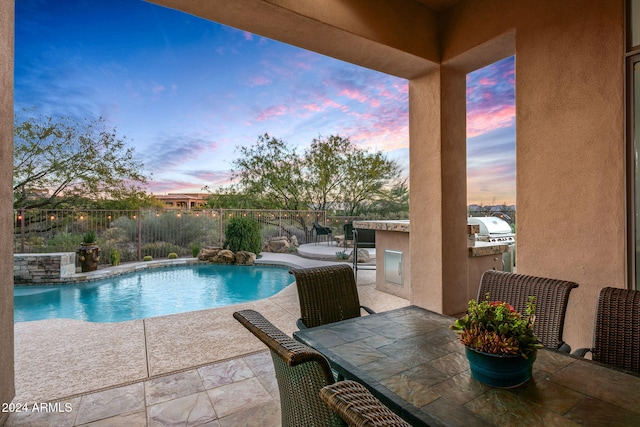 pool at dusk featuring an outdoor kitchen, a patio area, and grilling area