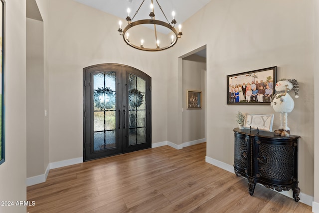 foyer with light hardwood / wood-style flooring, french doors, a high ceiling, and an inviting chandelier