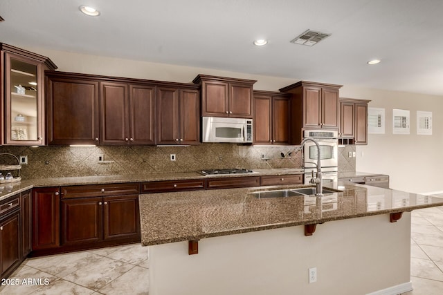 kitchen with stone countertops, stainless steel appliances, a breakfast bar, visible vents, and an island with sink