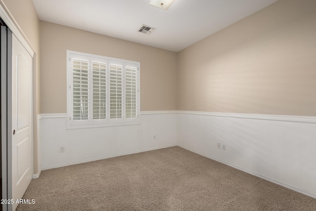 carpeted empty room featuring a wainscoted wall and visible vents