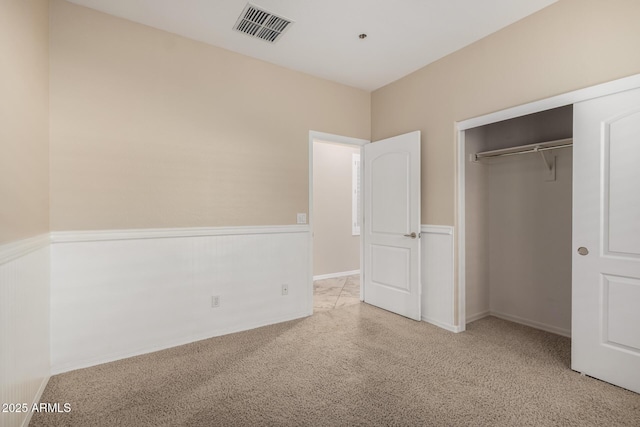 unfurnished bedroom featuring a wainscoted wall, visible vents, a closet, and light colored carpet