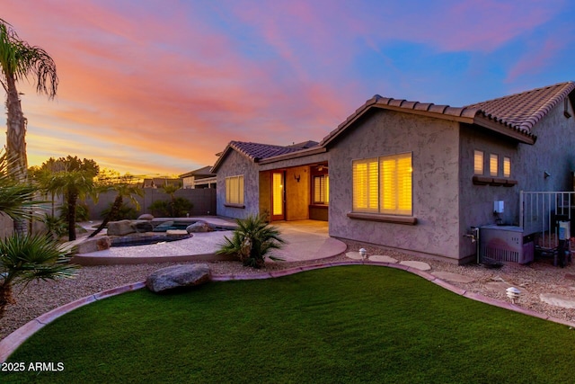 back of house at dusk featuring a lawn, a patio area, a tile roof, and stucco siding