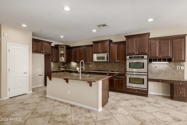 kitchen featuring stainless steel appliances, dark brown cabinetry, a sink, an island with sink, and a kitchen breakfast bar