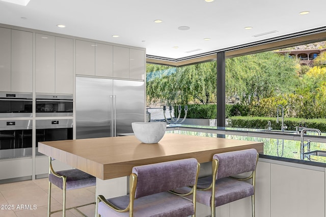 kitchen with light tile patterned flooring, stainless steel appliances, a kitchen breakfast bar, and sink