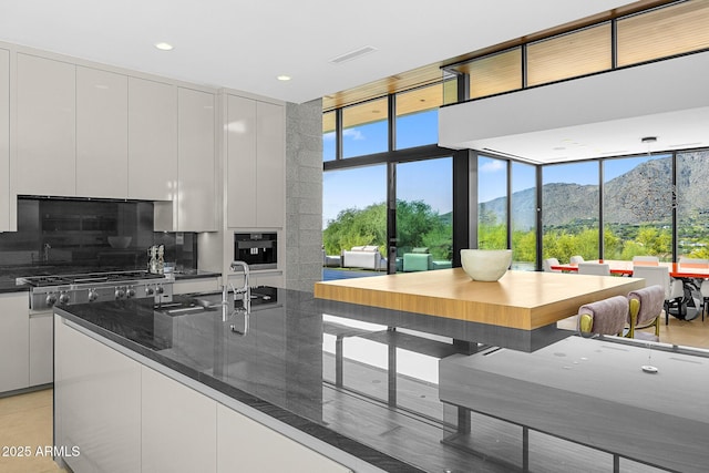 kitchen with decorative backsplash, a mountain view, white cabinets, and dark stone counters