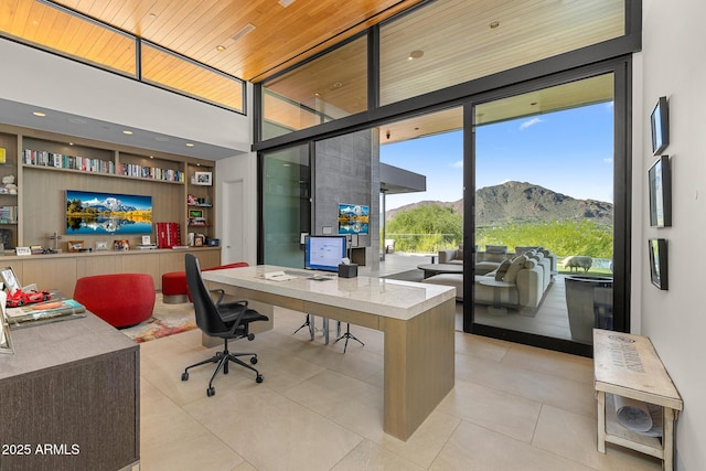 office space with wood ceiling, floor to ceiling windows, built in desk, light tile patterned flooring, and a mountain view