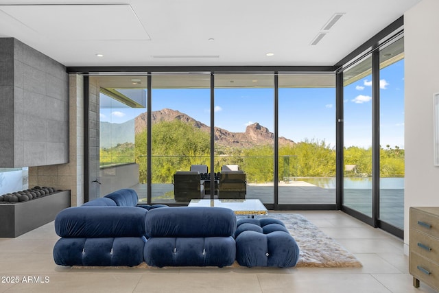 living room with a water and mountain view, light tile patterned flooring, floor to ceiling windows, and plenty of natural light