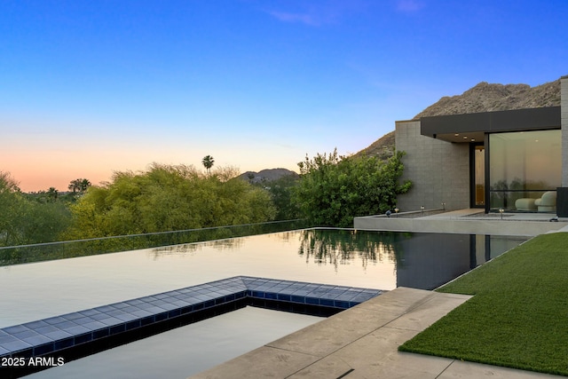 pool at dusk with a water view and a lawn