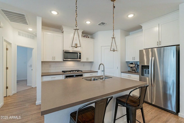 kitchen with a center island with sink, white cabinetry, sink, and appliances with stainless steel finishes