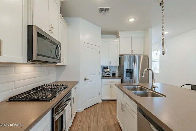 kitchen with white cabinetry, sink, stainless steel appliances, and decorative light fixtures