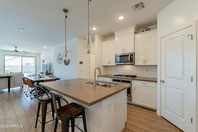 kitchen with white cabinets, appliances with stainless steel finishes, sink, and an island with sink