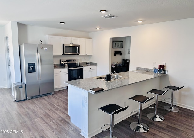kitchen featuring appliances with stainless steel finishes, a sink, light wood finished floors, a kitchen bar, and a peninsula