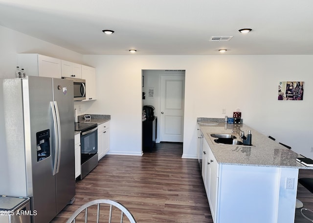 kitchen with appliances with stainless steel finishes, a sink, a peninsula, dark wood-style floors, and light stone countertops