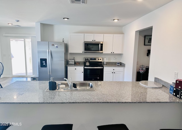 kitchen featuring stainless steel appliances, a sink, light stone countertops, and white cabinetry