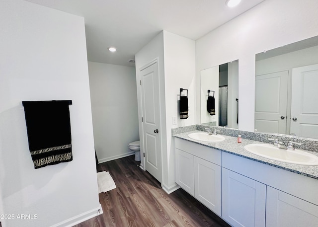 full bathroom featuring toilet, wood finished floors, double vanity, baseboards, and recessed lighting