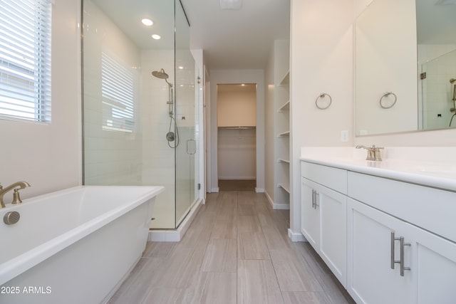 bathroom featuring a spacious closet, baseboards, a freestanding bath, a stall shower, and vanity