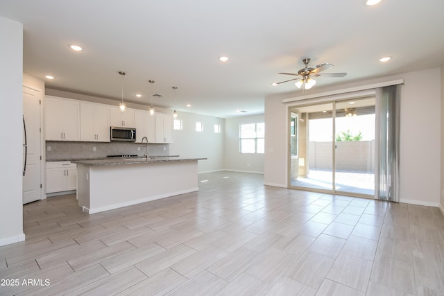 kitchen featuring stainless steel microwave, backsplash, ceiling fan, open floor plan, and white cabinets