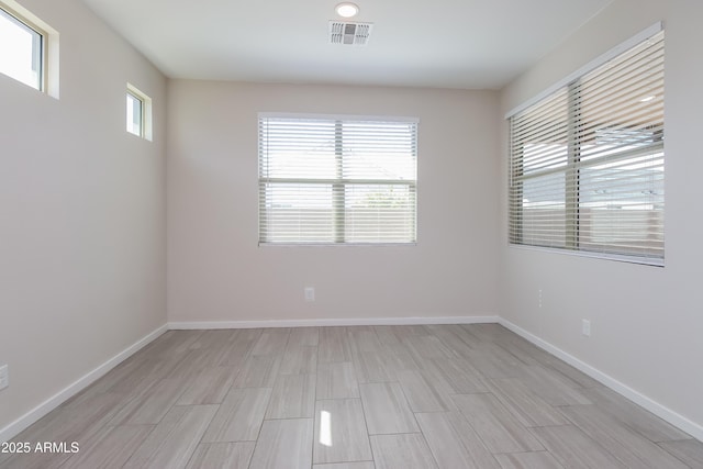 spare room featuring light wood-type flooring, visible vents, and baseboards