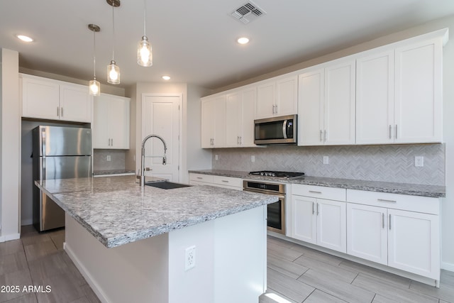 kitchen with visible vents, a kitchen island with sink, a sink, appliances with stainless steel finishes, and white cabinetry
