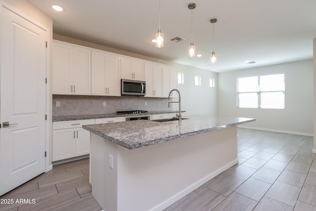 kitchen featuring stainless steel microwave, backsplash, visible vents, and a sink