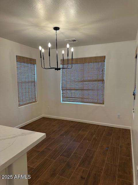 unfurnished dining area with visible vents, baseboards, a chandelier, and dark wood-style floors