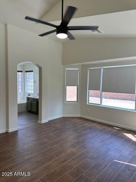 unfurnished room featuring arched walkways, dark wood finished floors, a ceiling fan, and lofted ceiling