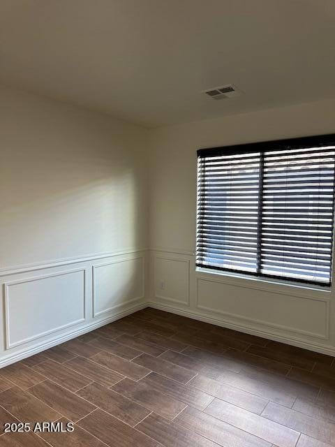 unfurnished room with wainscoting, a decorative wall, dark wood-type flooring, and visible vents