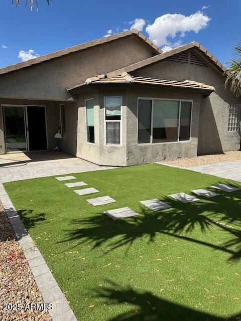 back of property featuring a yard, a patio, and stucco siding