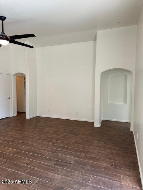 spare room featuring dark wood-type flooring, arched walkways, baseboards, and a ceiling fan