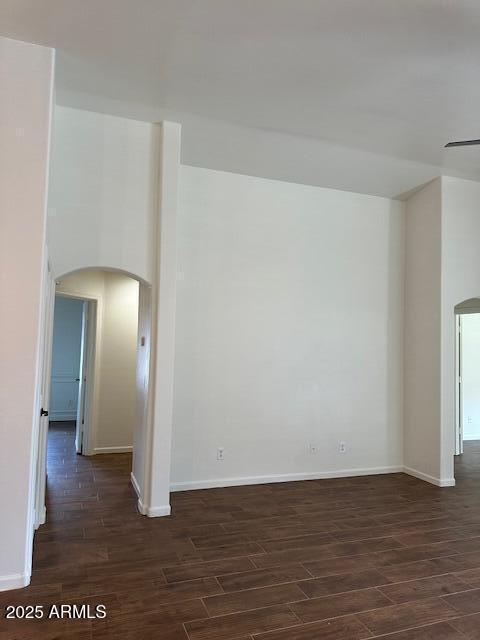 spare room featuring baseboards, arched walkways, and dark wood-style flooring