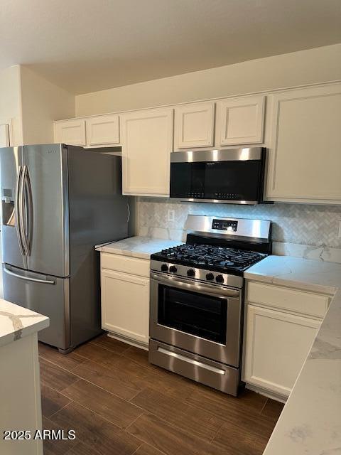 kitchen featuring white cabinets, stainless steel appliances, light stone countertops, and tasteful backsplash