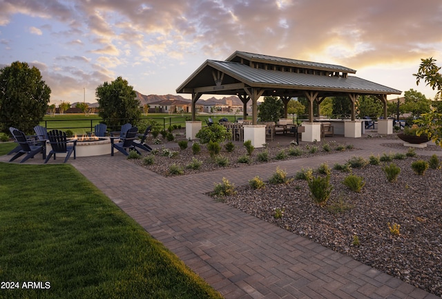 patio terrace at dusk featuring a gazebo, a fire pit, exterior kitchen, and a lawn