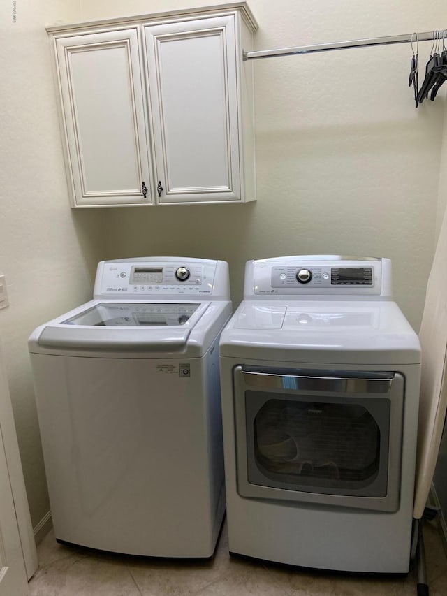 laundry room featuring cabinets, light tile patterned flooring, and separate washer and dryer