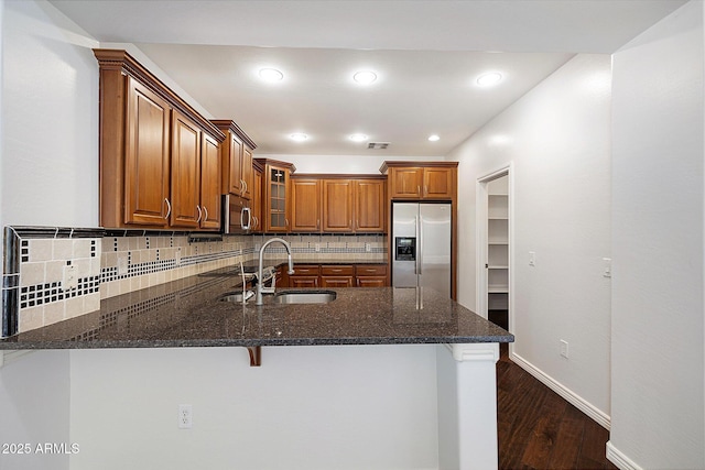 970 S Henry Ln, Gilbert, AZ 85296 - kitchen featuring appliances with stainless steel finishes, a peninsula, brown cabinetry, glass insert cabinets, and decorative backsplash