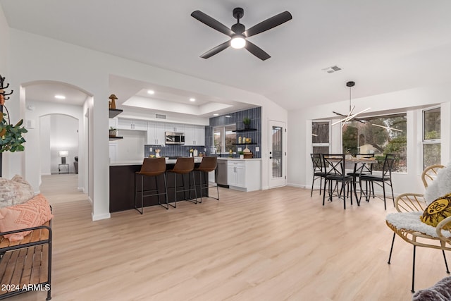 interior space with ceiling fan with notable chandelier, a tray ceiling, and light hardwood / wood-style flooring