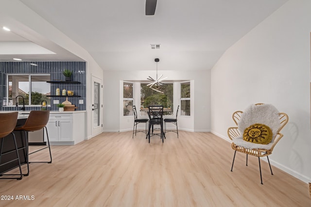 dining room featuring a chandelier, light wood-type flooring, a wealth of natural light, and lofted ceiling