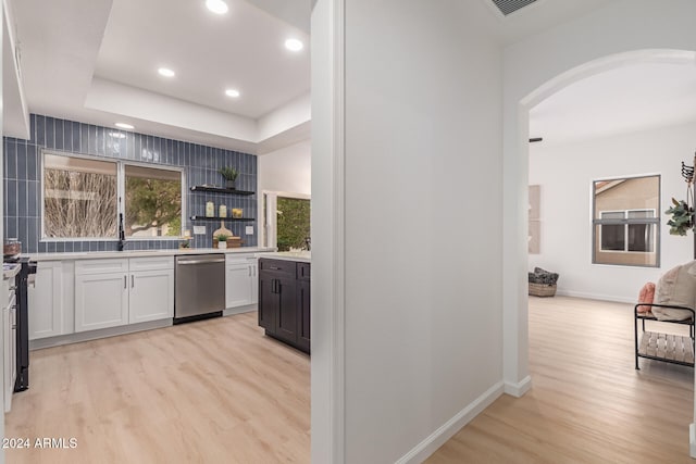 kitchen with light wood-type flooring, stainless steel dishwasher, a raised ceiling, range, and white cabinetry