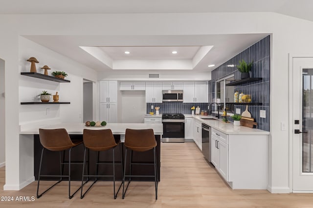 kitchen with white cabinetry, sink, a kitchen breakfast bar, light hardwood / wood-style floors, and appliances with stainless steel finishes