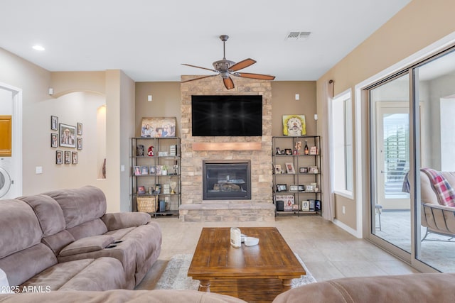 living room with ceiling fan, light tile patterned flooring, a stone fireplace, and washer / clothes dryer