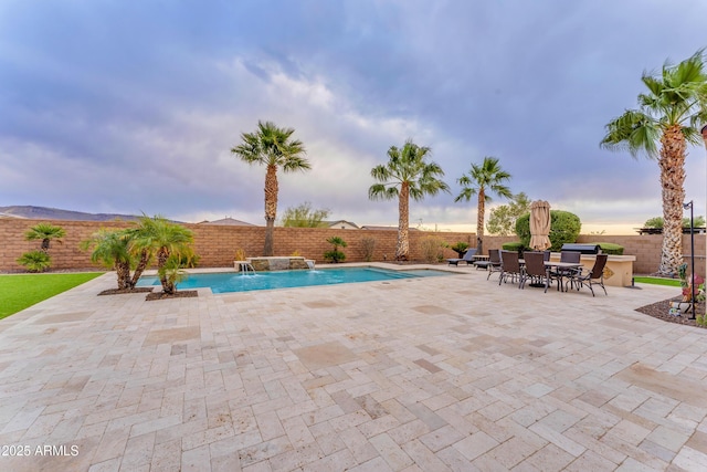 pool at dusk with pool water feature and a patio area