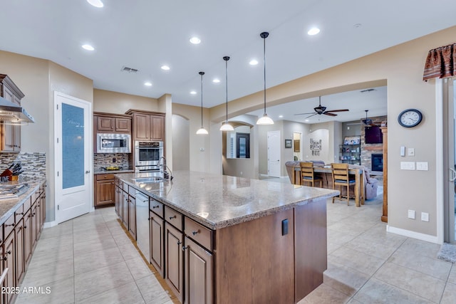 kitchen with sink, tasteful backsplash, appliances with stainless steel finishes, and an island with sink