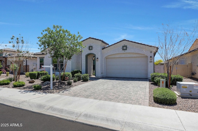 mediterranean / spanish house with a garage, fence, stucco siding, a tiled roof, and driveway