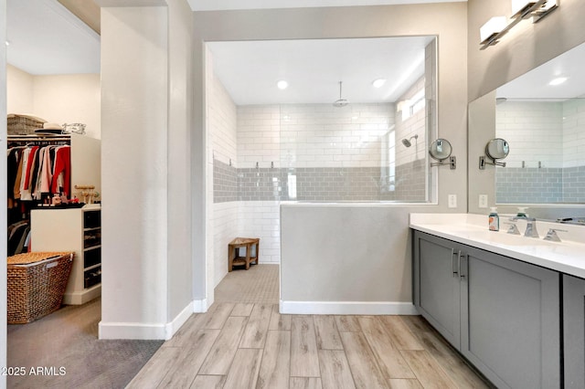bathroom featuring a walk in closet, wood finished floors, a walk in shower, baseboards, and vanity