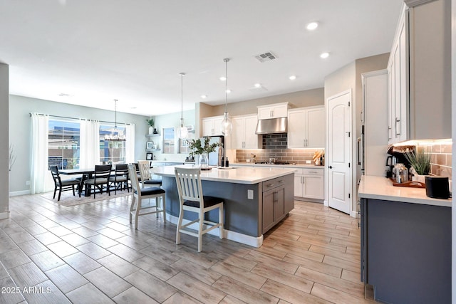 kitchen with under cabinet range hood, decorative backsplash, stainless steel gas stovetop, and light countertops