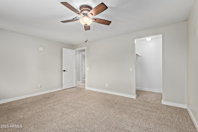 unfurnished bedroom featuring light colored carpet, a walk in closet, baseboards, and a ceiling fan