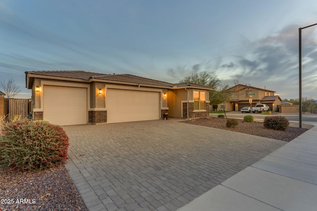 prairie-style home featuring a garage, stone siding, decorative driveway, and stucco siding