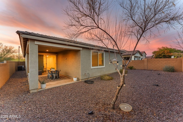 back of house at dusk featuring a patio area, a fenced backyard, and stucco siding